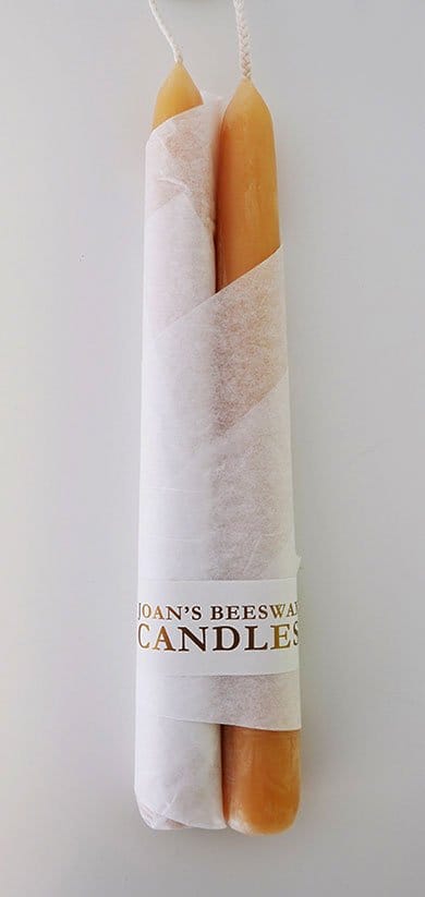 Two tall, cylindrical beeswax candles partially wrapped in white paper with the label 