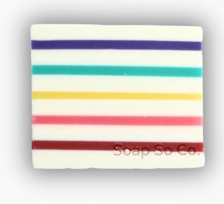 A rectangular white Soap So Co. bar featuring colorful horizontal stripes in purple, blue, teal, yellow, orange, and red, with 