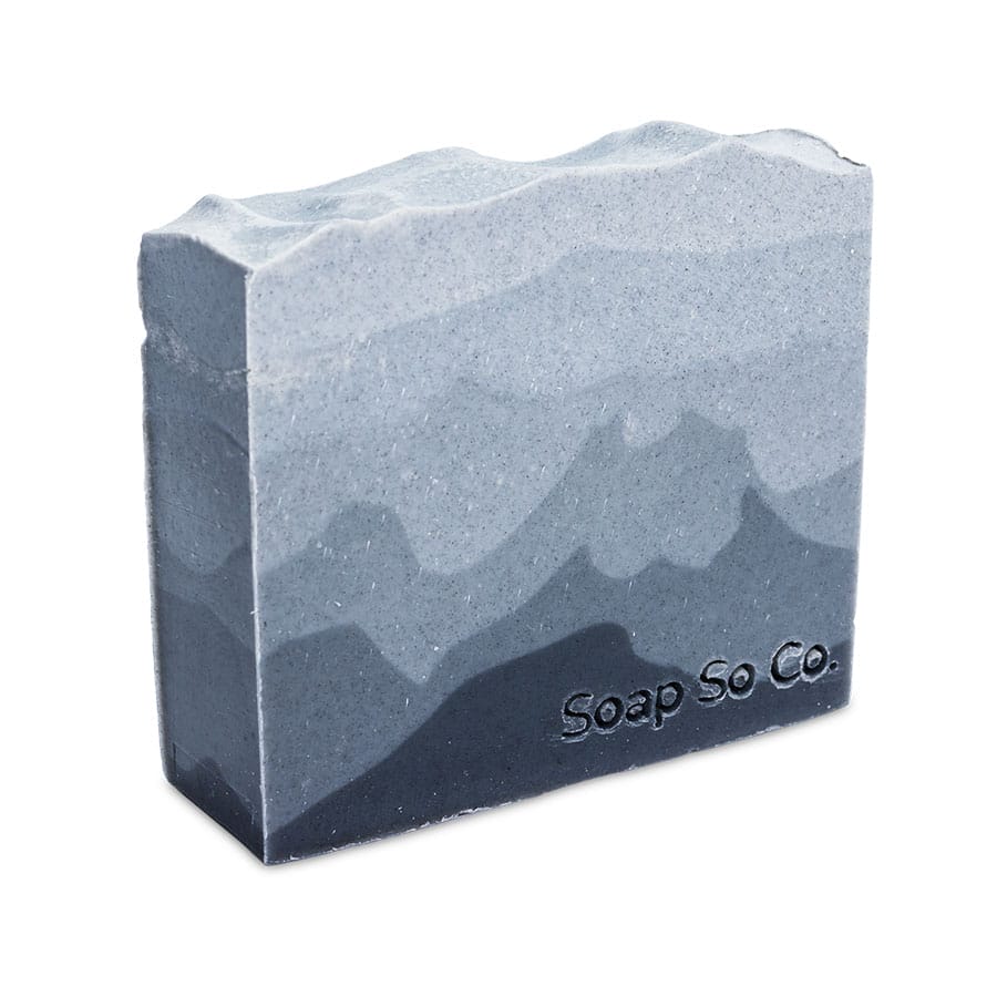The Soap So Co. bar features a textured pattern reminiscent of mountains, with its surface displaying multiple shades of gray for a layered effect. The brand name is embossed on the lower right corner of the soap.