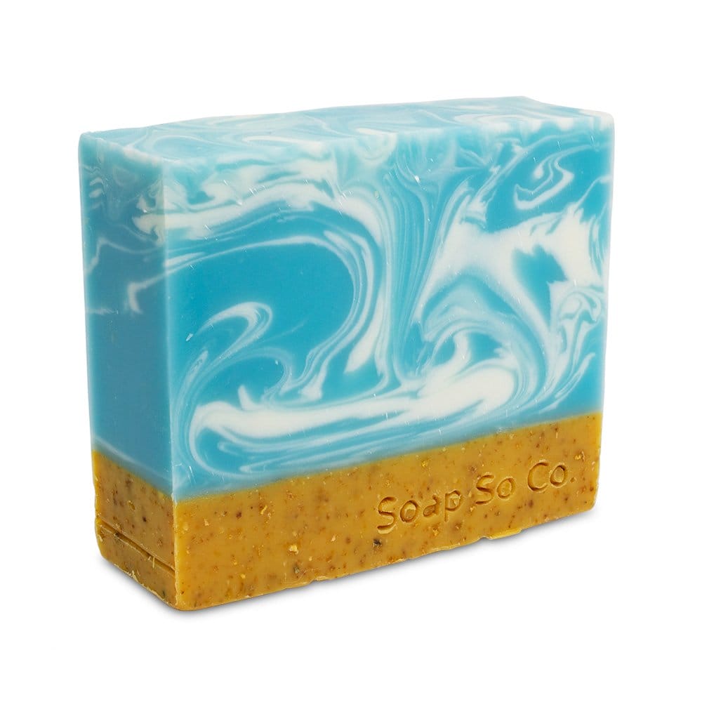 A handcrafted Soap So Co. bar features upper blue and white swirls reminiscent of waves, while the lower brown section has a grainy texture with