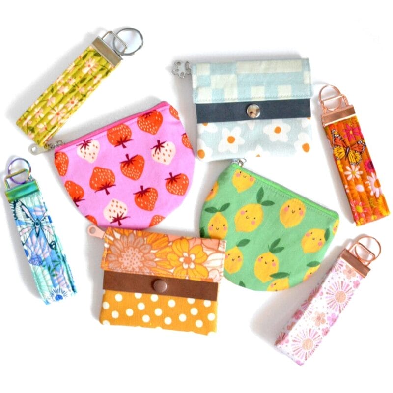 A vibrant assortment of colorful fabric pouches and key fobs, perfect for Holiday Bazaart 2024, arranged in a circular pattern. The pouches showcase patterns like strawberries and polka dots, while the key fobs feature striking floral and geometric designs.
