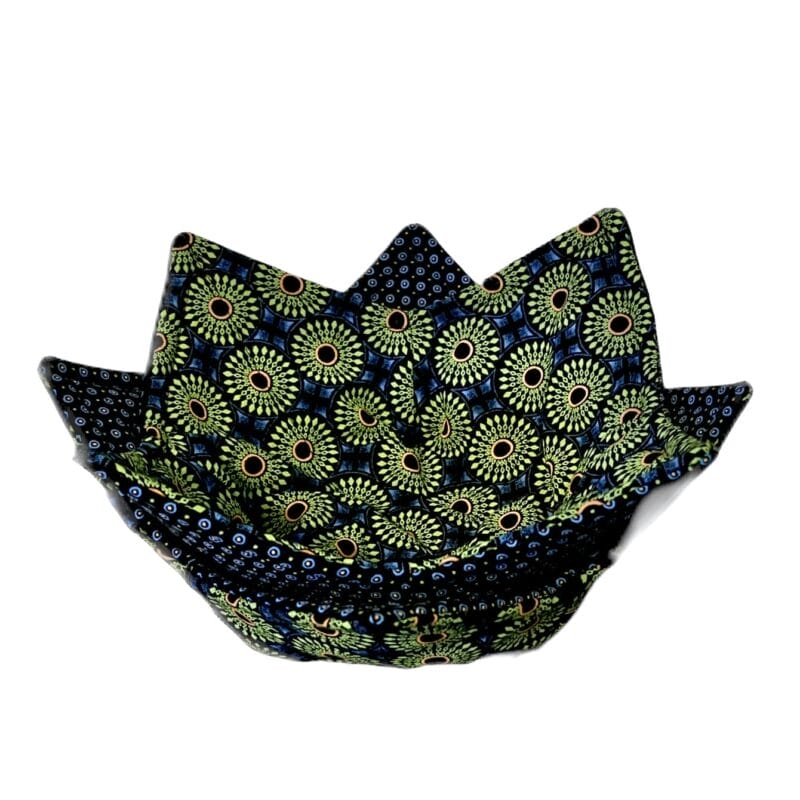 A charming fabric bowl with a geometric pattern in green, blue, and yellow colors. Perfect for your Holiday Bazaart 2024 collection, its design boasts circular motifs and small dots that form a star-like shape with pointed edges around the rim, adding festive flair.