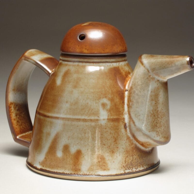 A ceramic teapot with a rounded body, wide angular handle, and long angled spout. The brown glaze with cream and light blue streaks gives it an earthy, rustic look—perfect for displaying at Bazaart 2025.