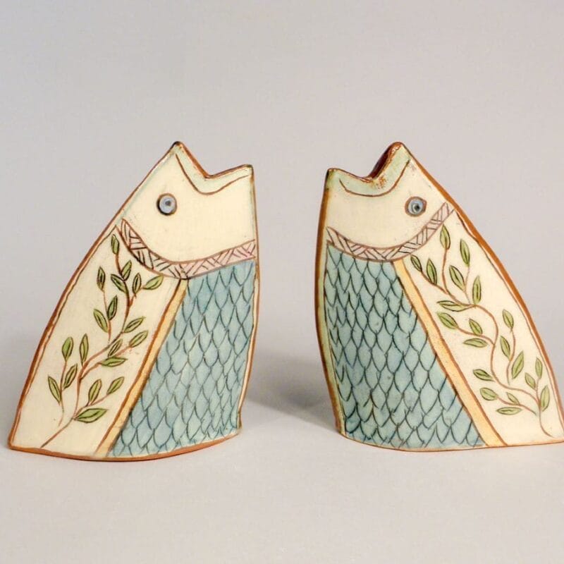 Two ceramic fish sculptures with blue scales, leaf patterns, and geometric designs face each other against a plain light background, capturing the artistic spirit of Bazaart 2025.
