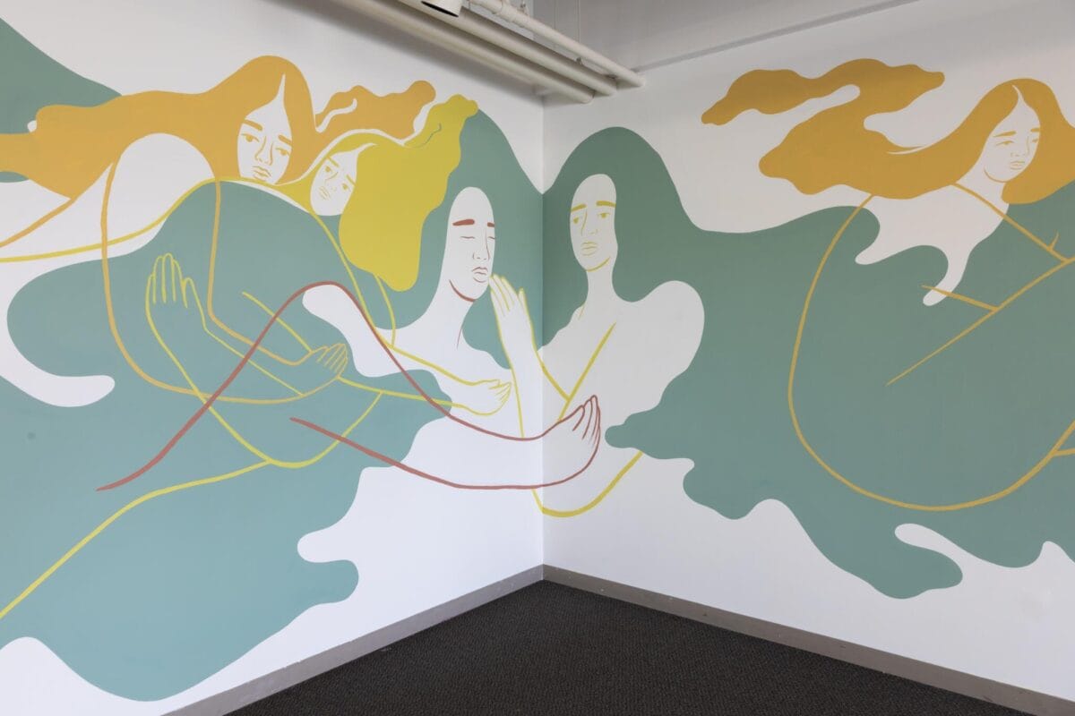 A corner room mural featuring stylized human figures. The figures are depicted in soft pastel colors and appear to blend into the walls, with fluid, elongated forms and calm expressions, creating a dreamlike and serene atmosphere.