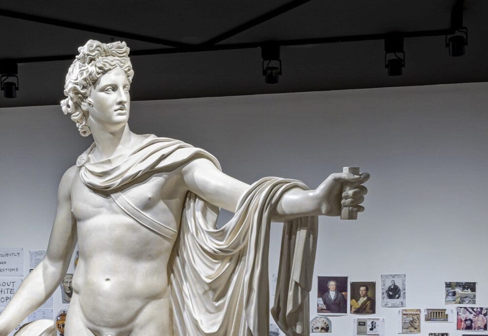 A Marble statue stands in front of a collage of images on the wall that make up a timeline.