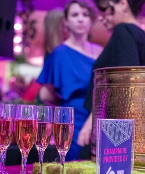 A close-up of a table with six glasses of champagne and a sign that reads 