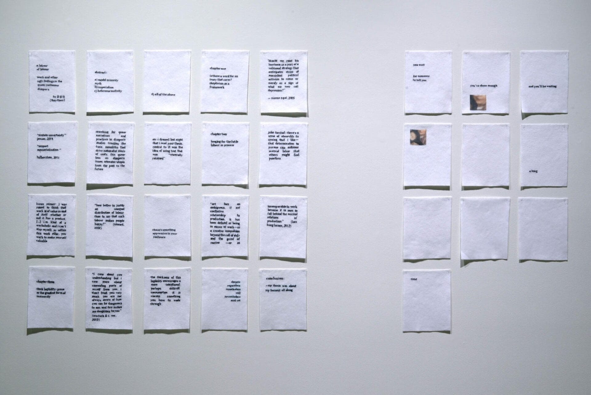 Image of multiple pieces of white paper with printed text, neatly arranged in a grid on a wall. The grid is divided into two sections: the left side contains five rows of five papers, and the right side contains six rows of three papers. Some text is visible.