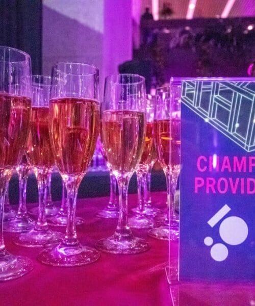 Champagne glasses displayed together on a table with sponsorship sign that notes 1080 Architecture as the sponsor
