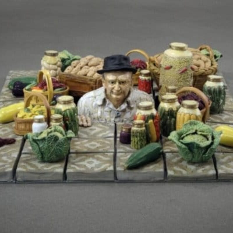 Ceramic vegetables surround a man in the middle. the man appears to be coming out of the flooring, we can only see from his shoulders up.