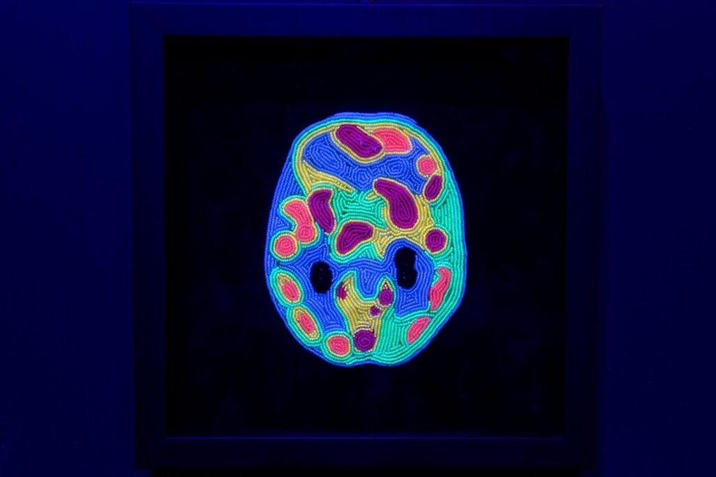A vibrant, glowing image of a brain scan in blue, green, red, and yellow hues is displayed in a dark frame against a shadowy background. The colors highlight brain activity so small we don't even think about it.