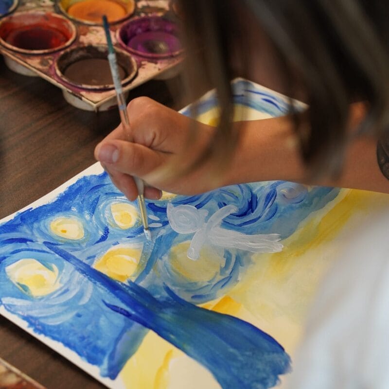A person paints a swirling blue and yellow scene on paper, inspired by Van Gogh's