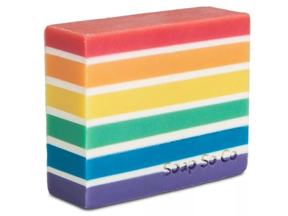 A rectangular bar of Soap So Co. soap with horizontal rainbow stripes, each in a different color, featuring embossed text that reads 