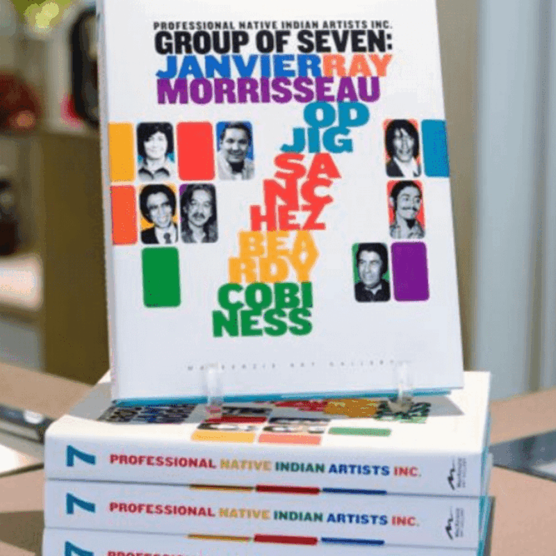 Une pile de quatre livres intitulée « Professional Native Indian Artists Inc: Group of Seven ». Le livre présente les noms et les photos de sept artistes sur sa couverture, avec des lettres colorées et audacieuses épelant leurs noms dans un design vertical et superposé.