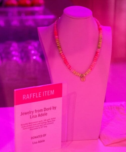 A mannequin bust is displayed on a table with a vibrant, multicolored beaded necklace draped over it. Next to the bust is a clear sign that reads 