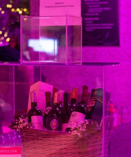 A raffle prize display featuring a basket filled with various wine bottles. The sign above invites attendees to 