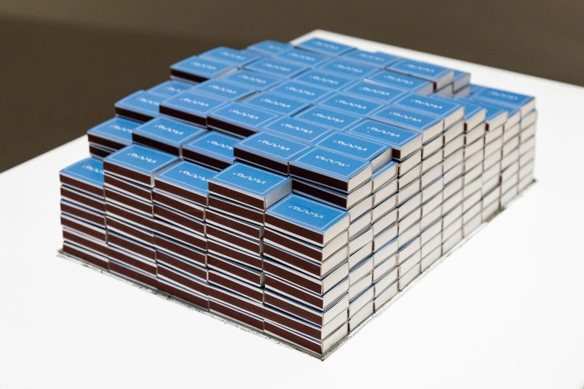 A neatly arranged stack of books forms a rectangular block on a white table. The covers, facing upwards, are blue with a white title. The spines are aligned, creating a uniform and organized appearance. The background is plain, emphasizing the stack.