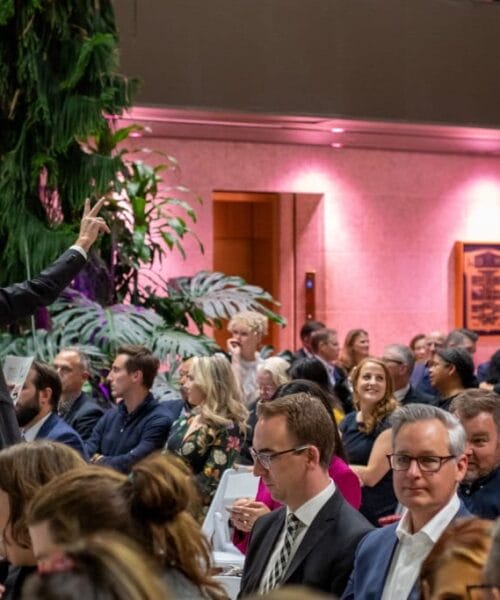 People seated for art auction. Auctioneer has one hand raised