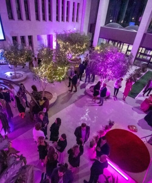 Wide shot looking over the balcony of the inside of the T.C. Douglas building lit by purple lights, people can be seen mingling