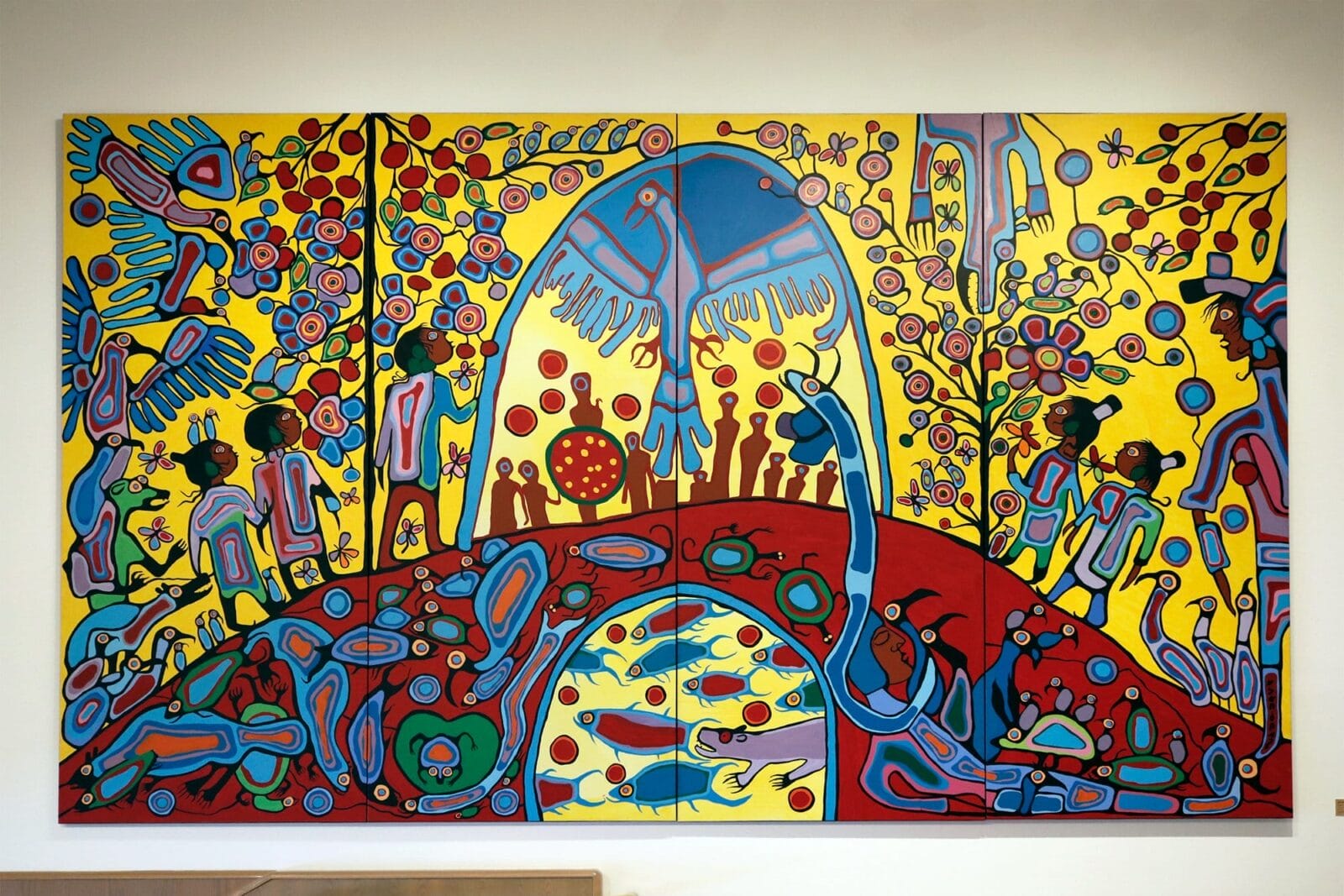 A vibrant, colorful mural depicting a surreal landscape with abstract human and animal figures. The artwork features a dominant central arch, bright yellow background, and intricate patterns in red, blue, and green, portraying various scenes of nature and community interaction.
