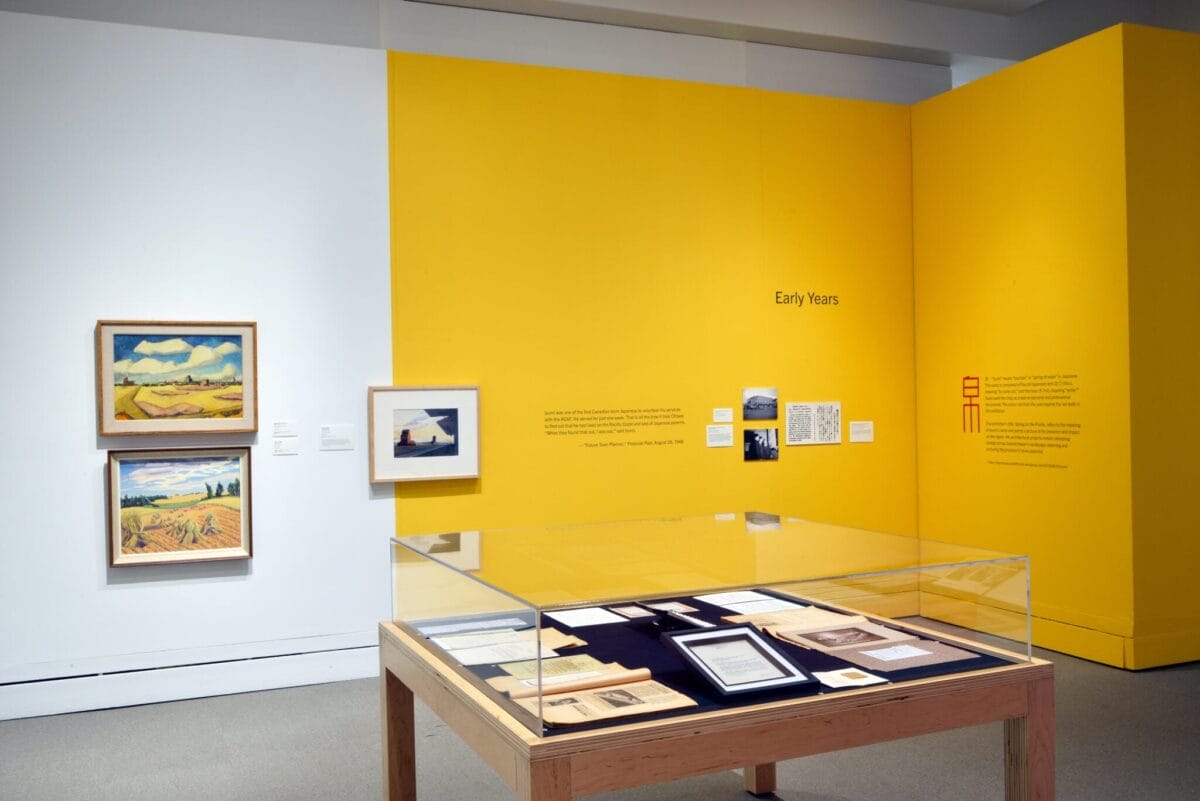 Une exposition intitulée « Les premières années » présente un mur jaune vif avec un texte descriptif. Des œuvres d'art encadrées sont exposées sur les murs adjacents. Une table d'exposition en bois présente des documents et des photographies sous une vitrine en verre.
