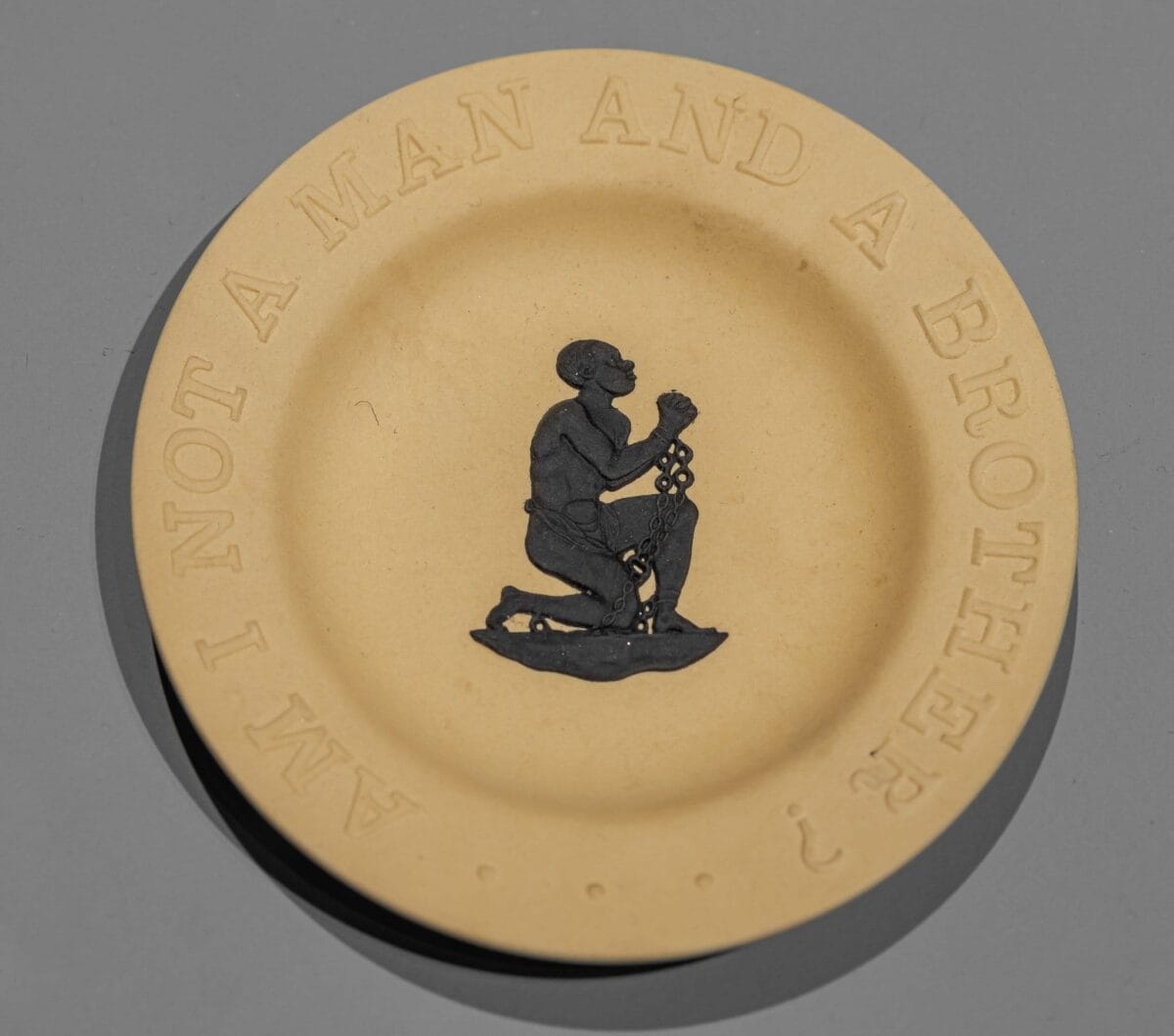 Photo of Anti-Slavery Medallion. Features the image of a man kneeling with text around the edges.
