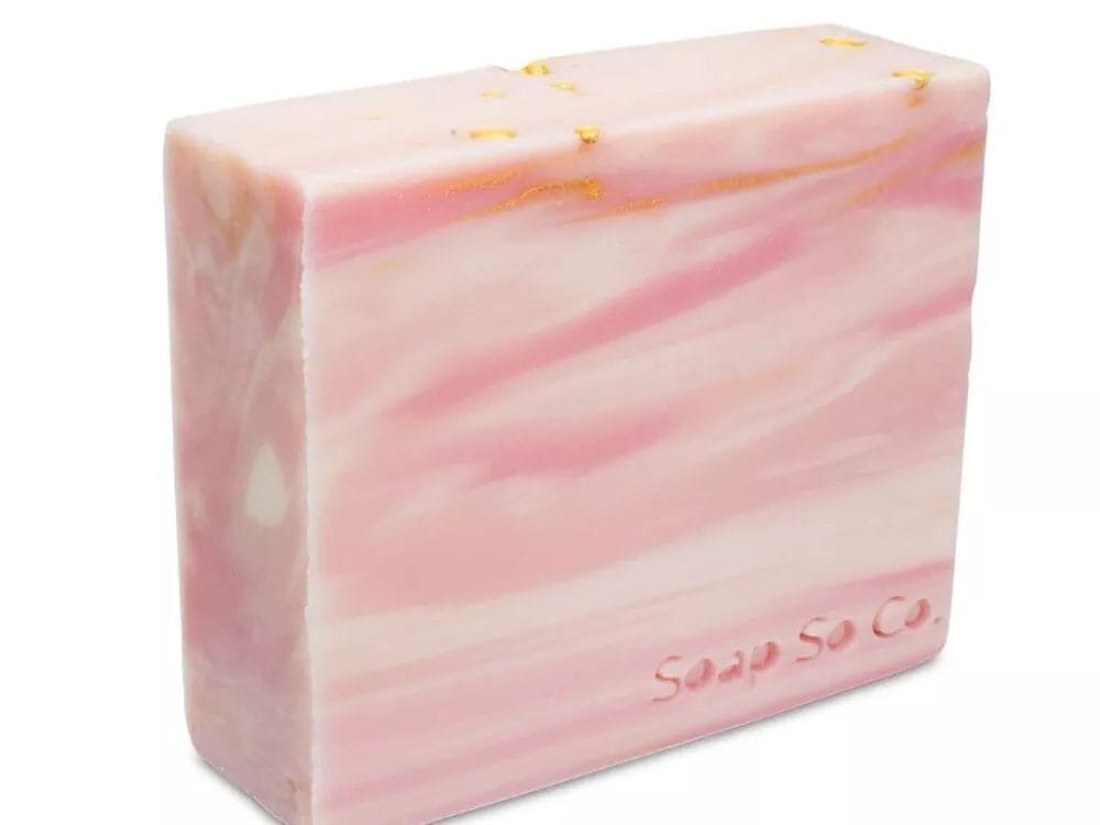 A rectangular bar of Soap So Co. soap features a stunning pink and white marbled pattern, complemented by elegant gold accents, with the brand name embossed on the side.
