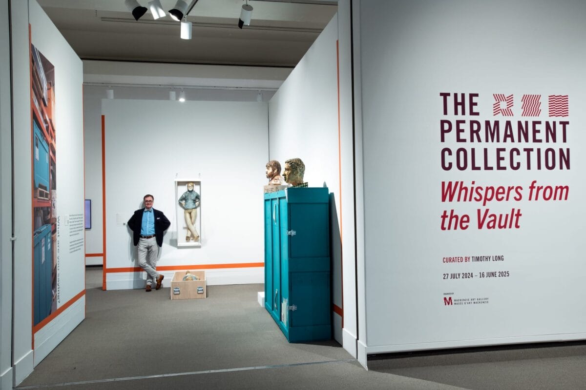 Une galerie de musée intitulée « La collection permanente : murmures du coffre-fort », organisée par Timothy Long, présentant divers objets et un homme appuyé contre un mur en arrière-plan.