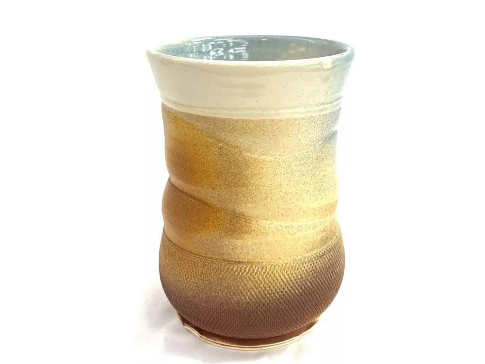 The Pink Charm Mug by PrairieMoon Handmade is a handmade ceramic cup with a textured surface, soft pink tones, gentle curves, and a glossy interior, displayed against a white background.