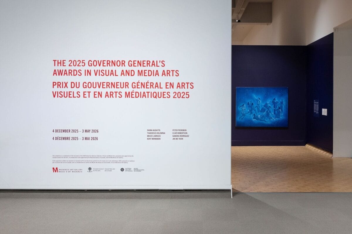 A museum wall displays text for The 2025 Governor General’s Awards in Visual and Media Arts in English and French; to the right, a blue artwork complements a blue wall in the adjacent room.