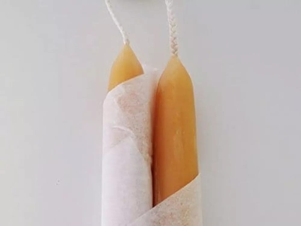 Two tall, cylindrical beeswax candles partially wrapped in white paper with the label 