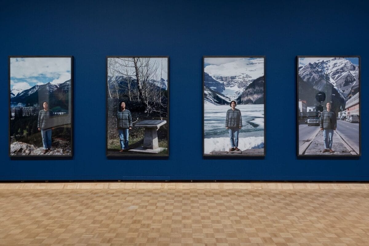 Four large framed photographs of a person in different outdoor mountain settings are displayed side by side on a dark blue wall, evoking the spirit of the 2025 Governor General’s Awards in Visual and Media Arts. The floor is light wood.