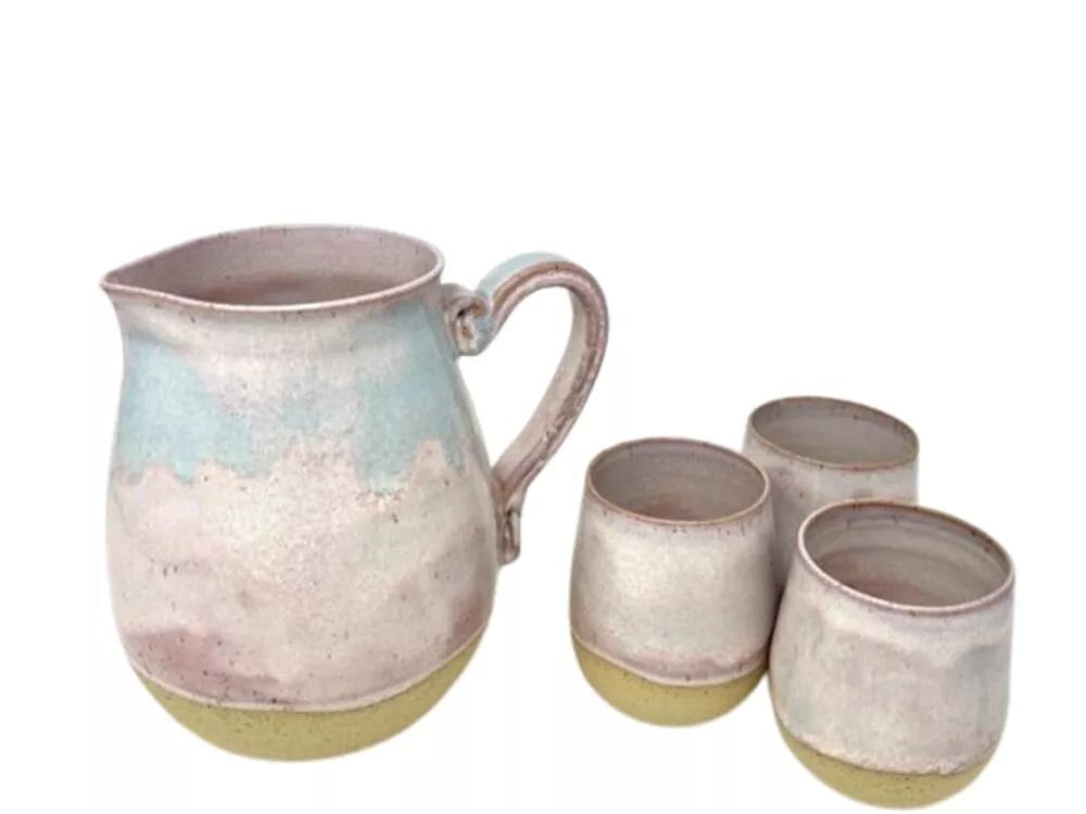The Pink Sky Pitcher by PrairieMoon Handmade includes a ceramic pitcher with handle and three matching cups, all in glossy pastel blue, pink, and beige. The rounded set boasts a handcrafted, rustic look.