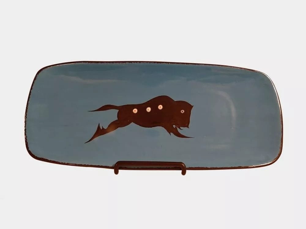 A Buffalo Platter by Veran Pardeahtan with a black fish design in the center, featuring three small white dots along the body. The plate is displayed on a stand against a plain white background.