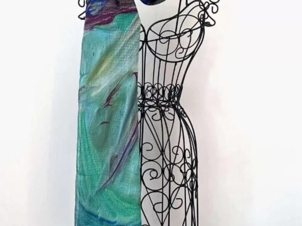 The Lariat Scarf by Kay Jay Studio, featuring an abstract pattern in teal, purple, and green, is displayed draped over a decorative black wire dress form against a plain white background.