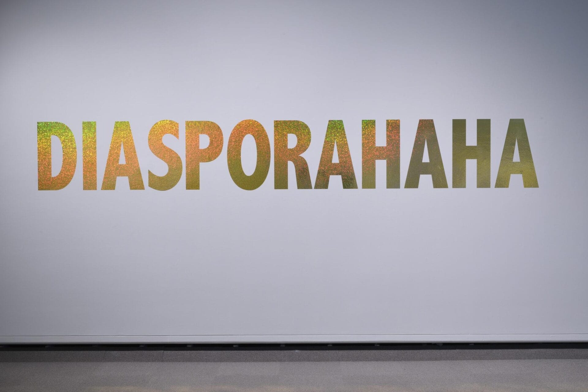 A white wall displays large text in a shimmering gradient of yellow and green, reading 